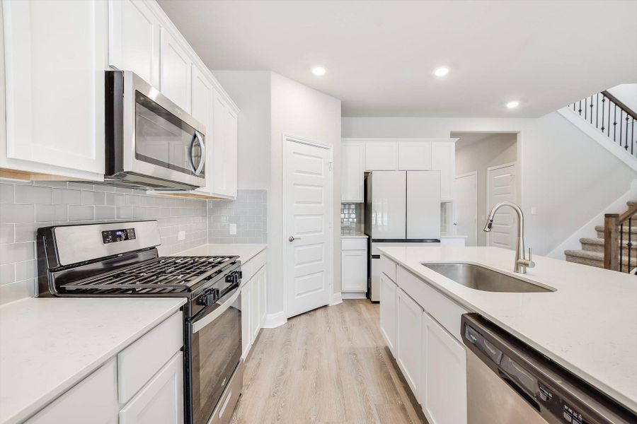 Kitchen with recessed lighting, appliances with stainless steel finishes, light wood-style floors, white cabinets, and a sink