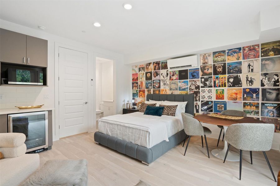 Bedroom with wine cooler, light wood-style floors, ensuite bath, recessed lighting, and an AC wall unit
