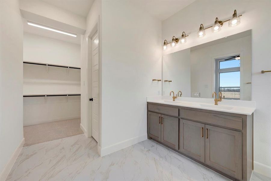 Bathroom featuring double vanity, a walk in closet, and light marble finish flooring Bathroom featuring double vanity, a walk in closet, and light marble finish flooring