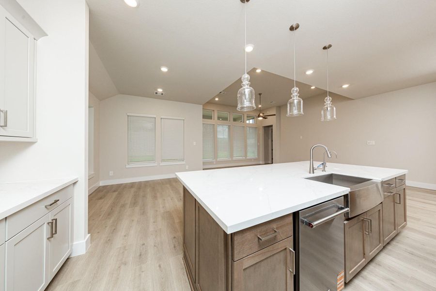 The kitchen island is a stunning centerpiece that anchors the space, while the layout provides a commanding view of the adjoining living areas and beyond. It features a seamless white quartz countertop that provides a vast workspace, complete with an integrated stainless steel apron-front farmhouse sink and a sleek, high-arc faucet.