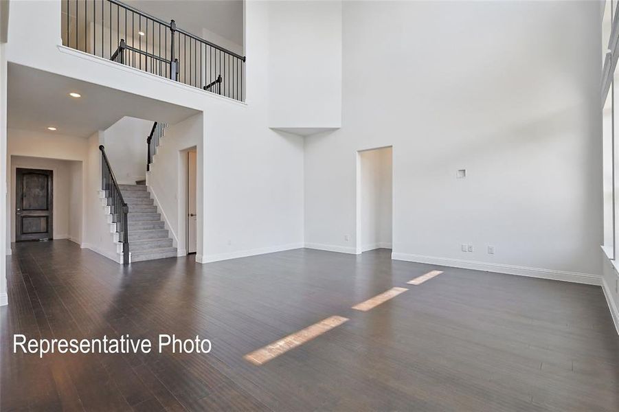 Great room featuring high ceilings, dark wood-finish flooring, a two-story staircase with dark balusters, and a second-story interior balcony