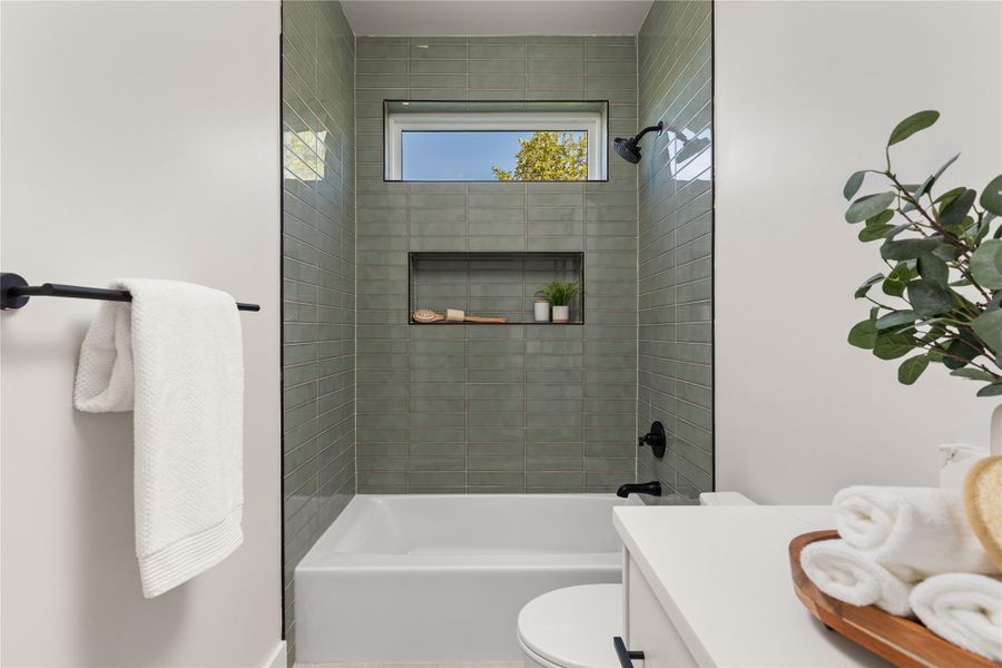 A high window brings natural light into the tiled shower and tub combination area.