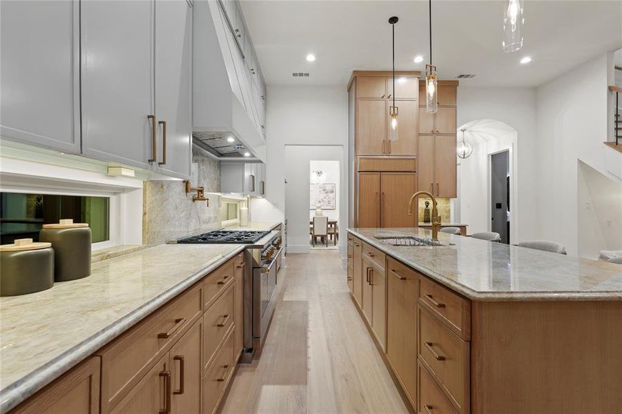 Kitchen with light stone counters, high quality appliances, arched walkways, hanging light fixtures, and light wood finished floors