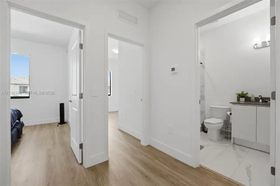 Wood-finish flooring throughout, white interior doors, and a bathroom featuring a vanity with a countertop, a wall-mounted light fixture, and tile flooring