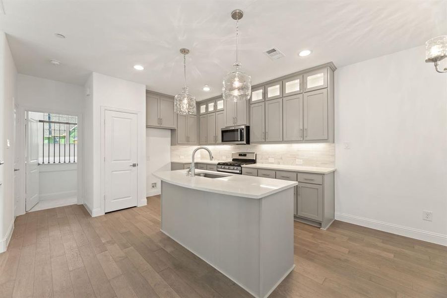 Kitchen featuring appliances with stainless steel finishes, sink, light wood-type flooring, decorative light fixtures, and a kitchen island with sink