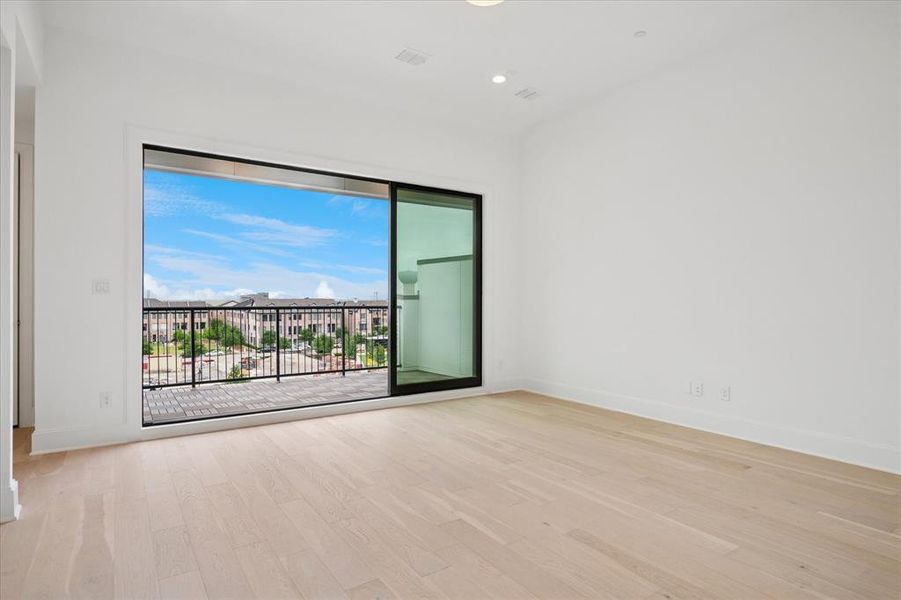 Spacious room featuring light wood-finish flooring, white walls, and a large sliding glass door