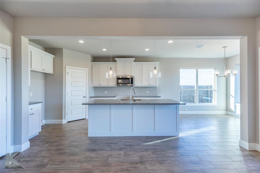 Kitchen with dark stone counters, backsplash, light wood-style flooring, white cabinets, and hanging light fixtures