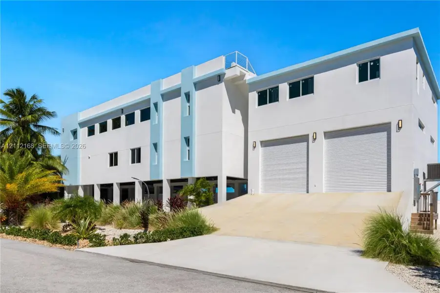 Multi-story contemporary exterior featuring a concrete facade, dual roll-up garage doors, a concrete vehicle ramp, and exterior wall-mounted lighting Multi-story contemporary exterior featuring a concrete facade, dual roll-up garage doors, a concrete vehicle ramp, and exterior wall-mounted lighting