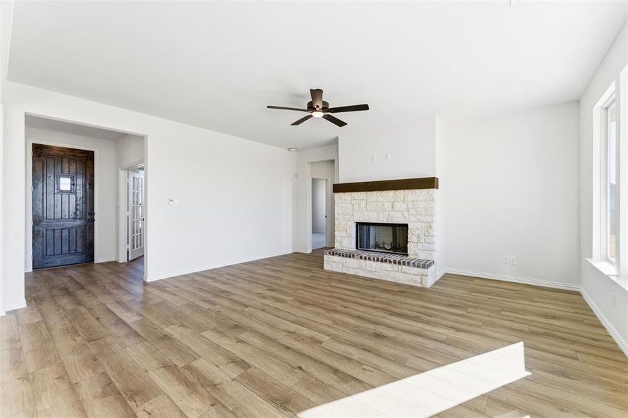 Unfurnished living room featuring plenty of natural light, ceiling fan, light wood-type flooring, and a stone fireplace