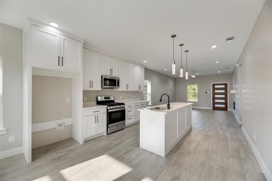 Kitchen with white cabinets, an island with sink, appliances with stainless steel finishes, decorative light fixtures, and sink