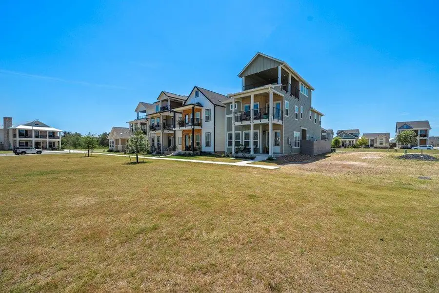 Multi-level coastal architecture faces a wide grassy common area under clear blue skies. Multi-level coastal architecture faces a wide grassy common area under clear blue skies.