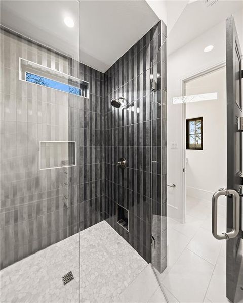 Contemporary shower enclosure featuring full-height glass panels, vertical two-tone tile, a built-in shower niche, and pebble-tile flooring