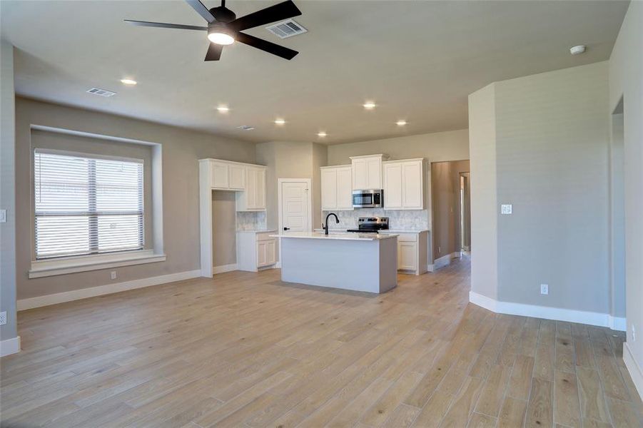 Kitchen featuring backsplash, white cabinets, open floor plan, ceiling fan, and stainless steel appliances