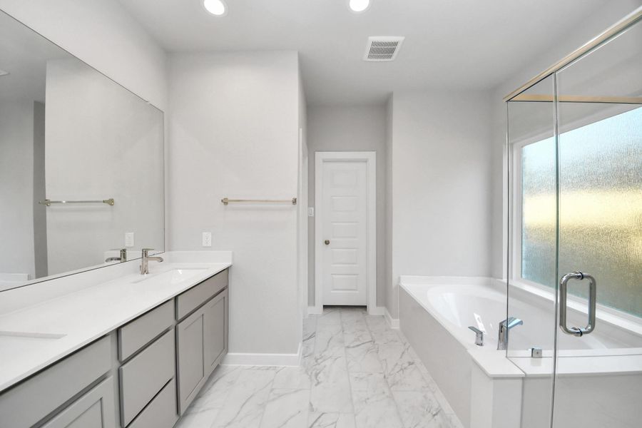 Escape to a spa-like oasis in this primary bathroom. Enjoy a walk-in shower with tile surround, a separate garden tub with custom detailing, and an elegant vanity featuring light countertops, modern hardware, and beautiful recessed lights. Experience luxury and relaxation in every detail. Sample photo of completed home with similar floor plan. Actual colors and selections may vary. Escape to a spa-like oasis in this primary bathroom. Enjoy a walk-in shower with tile surround, a separate garden tub with custom detailing, and an elegant vanity featuring light countertops, modern hardware, and beautiful recessed lights. Experience luxury and relaxation in every detail. Sample photo of completed home with similar floor plan. Actual colors and selections may vary.