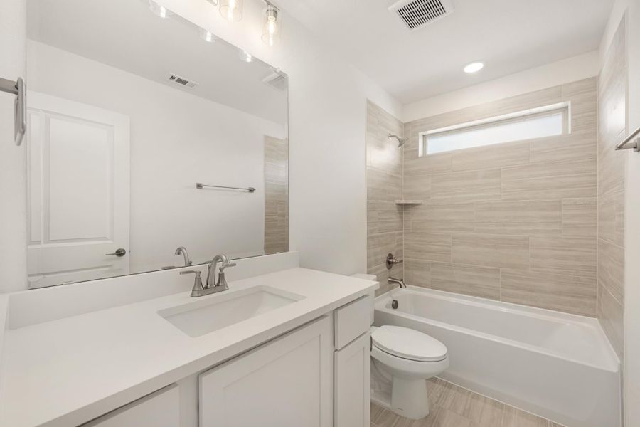 Bathroom with white vanity, large mirror, and tiled tub-shower combo with small window