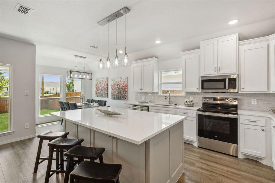 Kitchen with white cabinetry, stainless steel appliances, hanging light fixtures, decorative backsplash, and light hardwood / wood-style floors