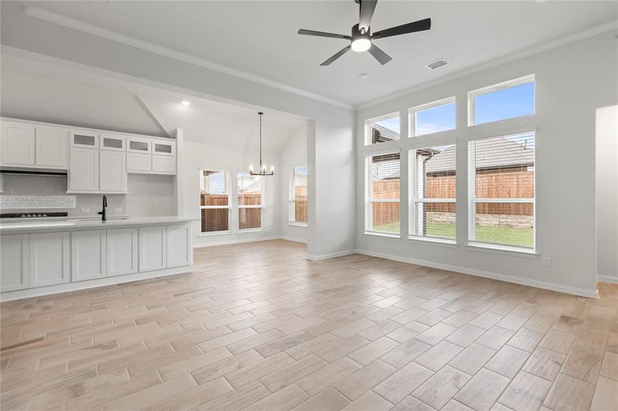 Unfurnished living room with ceiling fan with notable chandelier, light hardwood / wood-style flooring, sink, and ornamental molding