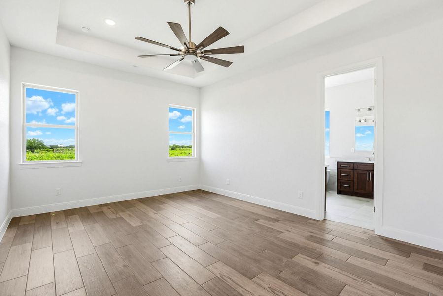 Sun-filled primary bedroom with a contemporary ceiling fan and views of lush greenery.