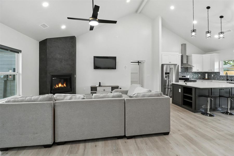 Living area featuring light wood-type flooring, high vaulted ceiling, a fireplace, ceiling fan, and beam ceiling