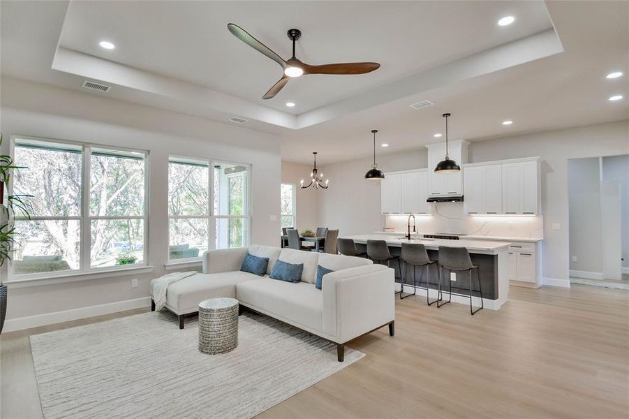 Living area featuring a tray ceiling, a chandelier, light wood finished floors, ceiling fan, and recessed lighting Living area featuring a tray ceiling, a chandelier, light wood finished floors, ceiling fan, and recessed lighting