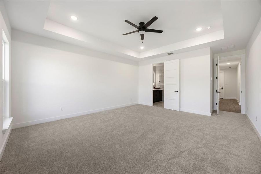 Spacious room featuring tray ceilings with recessed lighting, a ceiling fan, and light-toned carpeting Spacious room featuring tray ceilings with recessed lighting, a ceiling fan, and light-toned carpeting