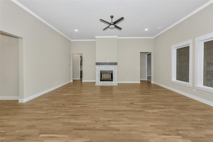 Unfurnished living room featuring a tile fireplace, ceiling fan, light hardwood / wood-style flooring, and ornamental molding