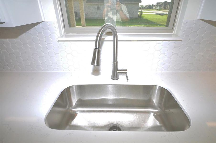 Undercounted single bowl sink with a bright window beyond.