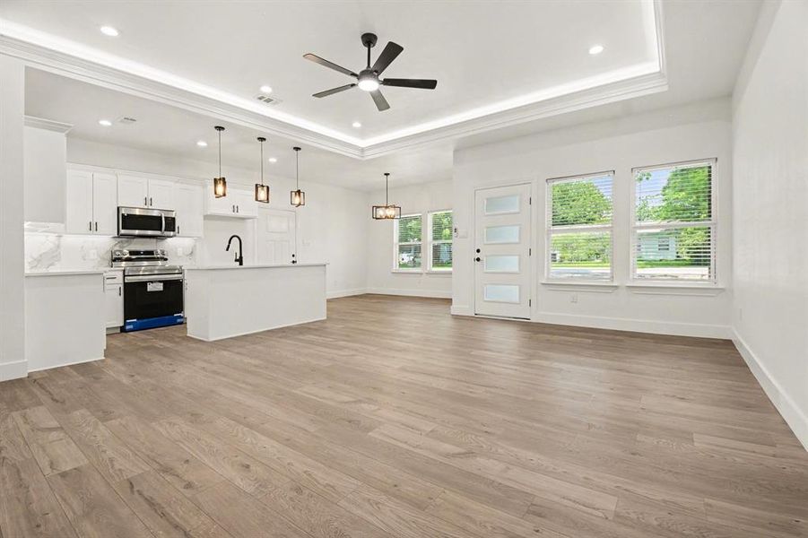 The property features an open-concept living space with light-colored flooring, a modern kitchen with white cabinetry and stainless steel appliances, and a ceiling fan