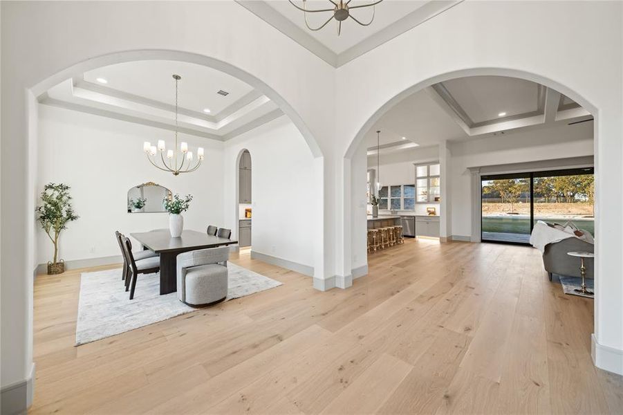 Dining space featuring a chandelier, light wood-type flooring, a raised ceiling, and arched walkways Dining space featuring a chandelier, light wood-type flooring, a raised ceiling, and arched walkways