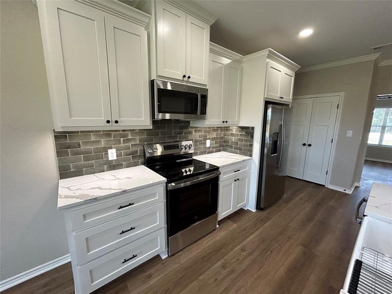 Kitchen with stainless steel appliances, ornamental molding, white cabinets, decorative backsplash, and light stone countertops