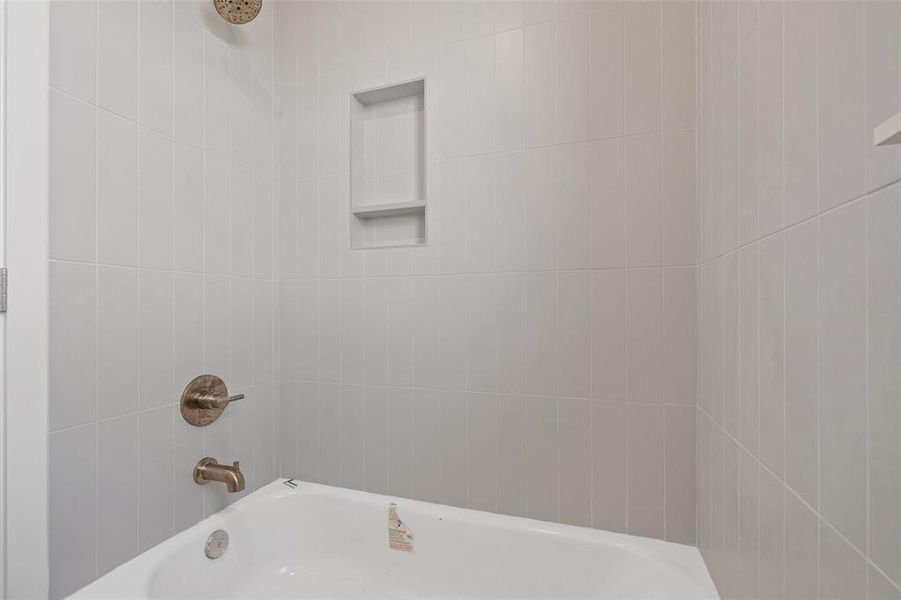 Bathtub with white subway tile surround, integrated shower niche, and brushed brass fixtures