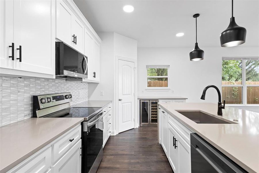 Kitchen with stainless steel appliances, white cabinets, wine cooler, decorative light fixtures, and recessed lighting