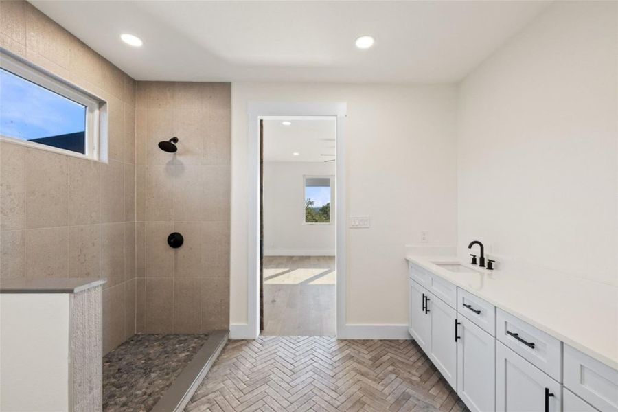 Modern bathroom featuring a tiled shower, herringbone floor, and a sleek vanity with ample counter space. Modern bathroom featuring a tiled shower, herringbone floor, and a sleek vanity with ample counter space.