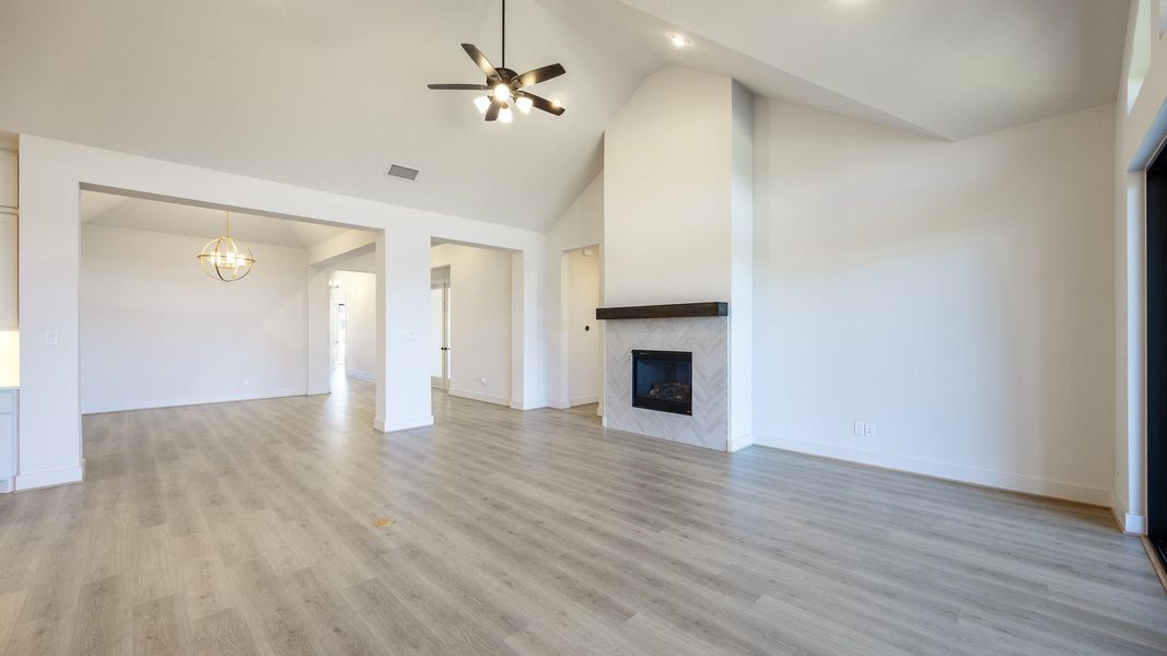 Unfurnished living room featuring high vaulted ceiling, light wood-type flooring, ceiling fan, a high end fireplace, and a chandelier Unfurnished living room featuring high vaulted ceiling, light wood-type flooring, ceiling fan, a high end fireplace, and a chandelier