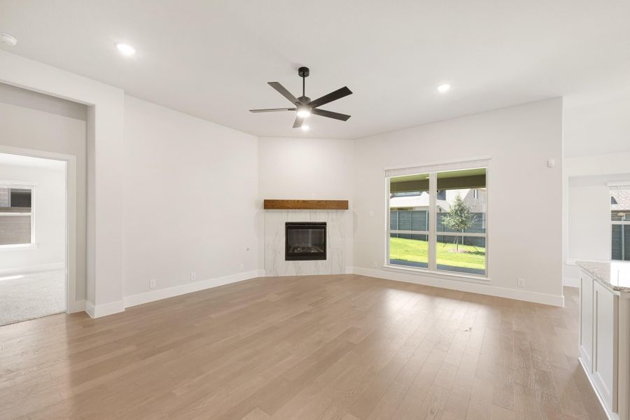 Open living room with light wood floors, marble fireplace, wood mantel, and ceiling fan