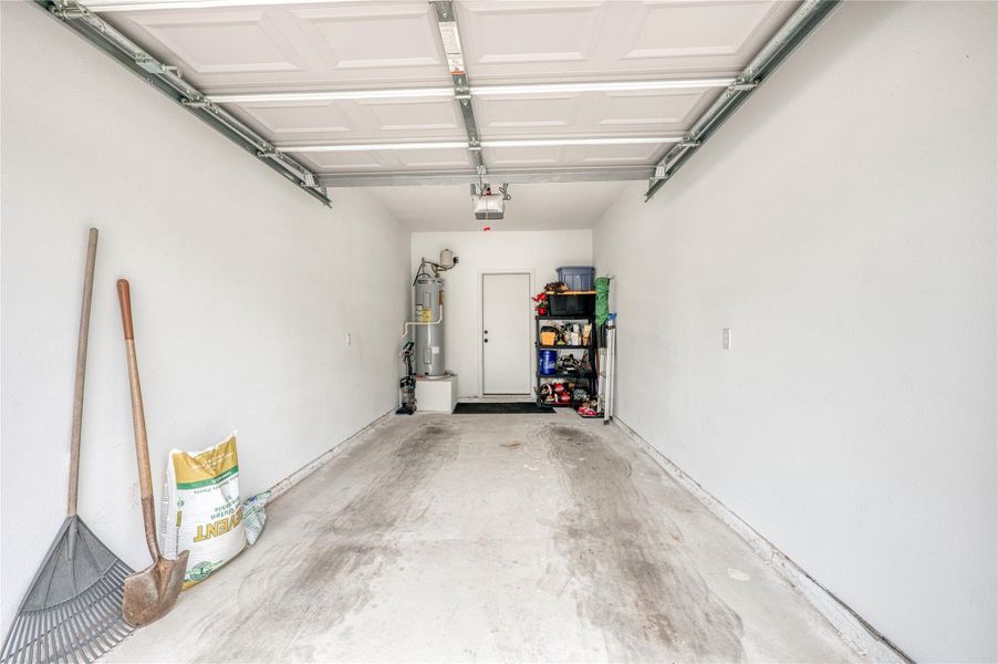 Spacious garage with a white panel garage door, painted white walls, and a dedicated utility area