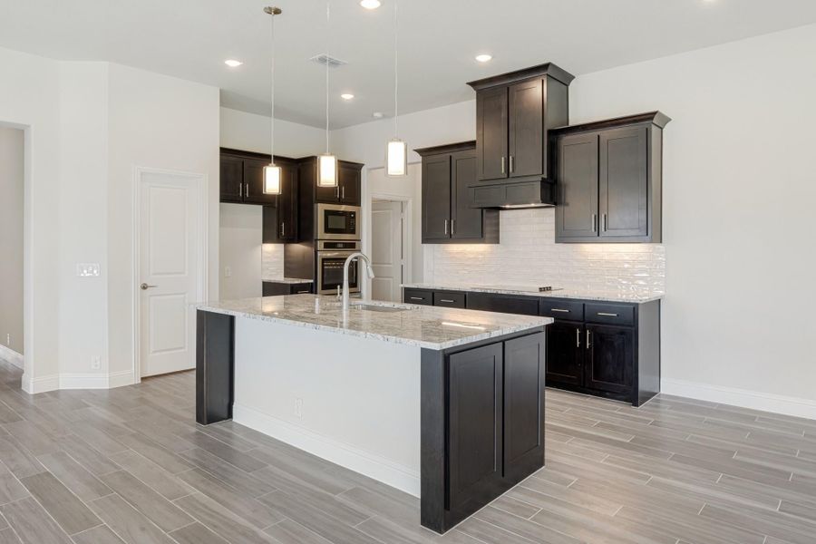 Kitchen with dark cabinets, granite island, pendant lights, and tile backsplash on wood-look floors Kitchen with dark cabinets, granite island, pendant lights, and tile backsplash on wood-look floors