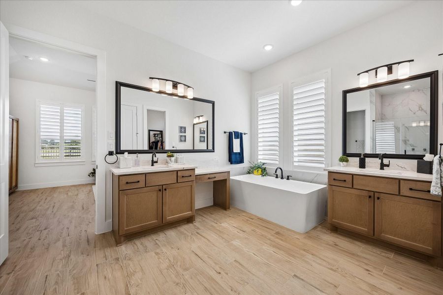 This primary suite showcases seamless wood-plank tile flooring extending from the bedroom into the bathroom. The spa-like primary bath features custom soft close dual granite countertop vanities, a dedicated makeup station for seating, and an upgraded freestanding soaking tub accented by sleek matte black hardware. Custom plantation shutters complete the space, offering both elegance and enhanced privacy.