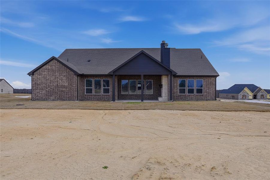 Back of property with a chimney, a patio area, brick siding, and roof with shingles