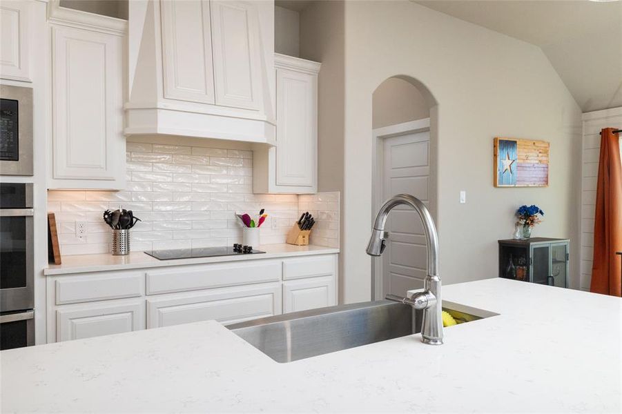 Kitchen with white cabinets, premium range hood, decorative backsplash, light stone countertops, and vaulted ceiling
