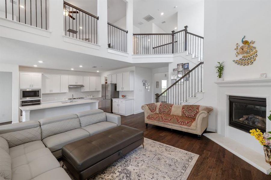 Living area featuring dark wood-style flooring, recessed lighting, visible vents, a glass covered fireplace, and stairs