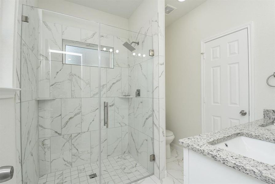 Modern bathroom with marble tiles, glass shower enclosure, granite countertop, and white cabinetry.