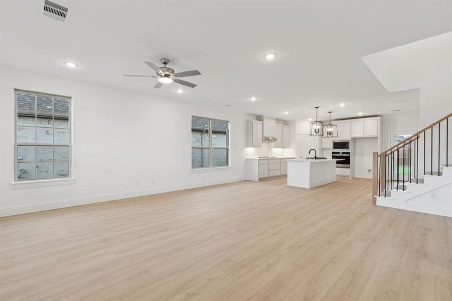 Unfurnished living room featuring stairs, light wood finished floors, recessed lighting, and a ceiling fan Unfurnished living room featuring stairs, light wood finished floors, recessed lighting, and a ceiling fan