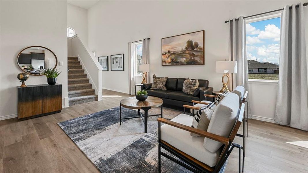 Living area featuring light wood-type flooring, a towering ceiling, and stairs Living area featuring light wood-type flooring, a towering ceiling, and stairs