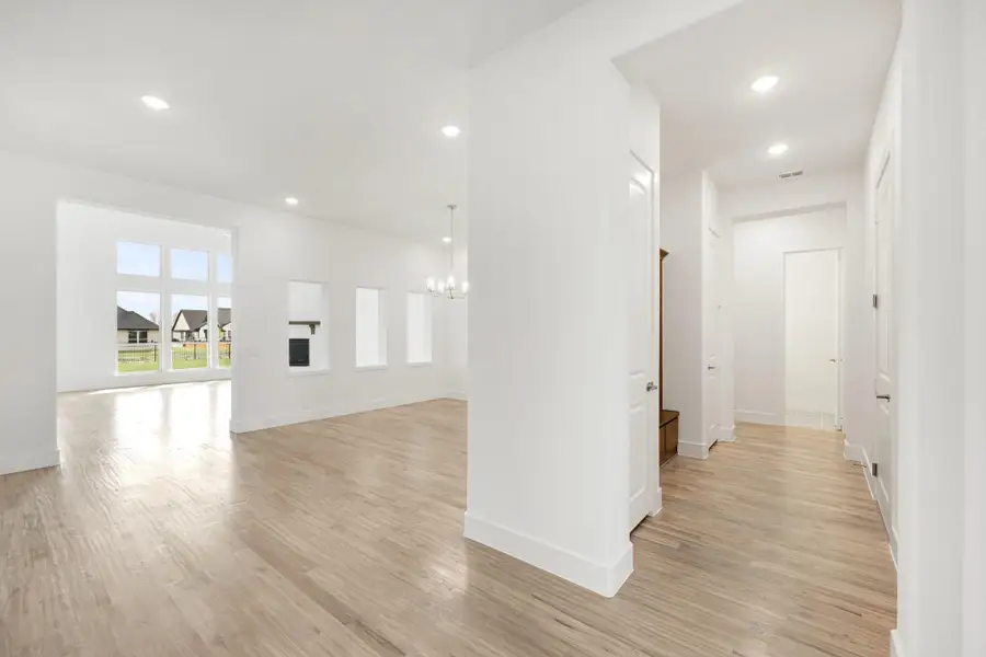Open living area and hallway with light hardwood floors, white walls, recessed lighting, and a chandelier Open living area and hallway with light hardwood floors, white walls, recessed lighting, and a chandelier