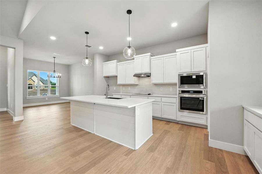 Kitchen featuring appliances with stainless steel finishes, under cabinet range hood, backsplash, white cabinets, and light wood finished floors Kitchen featuring appliances with stainless steel finishes, under cabinet range hood, backsplash, white cabinets, and light wood finished floors