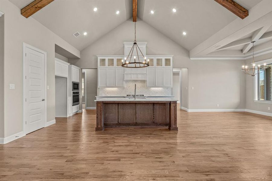 Kitchen featuring a chandelier, beam ceiling, open floor plan, white cabinetry, and glass insert cabinets