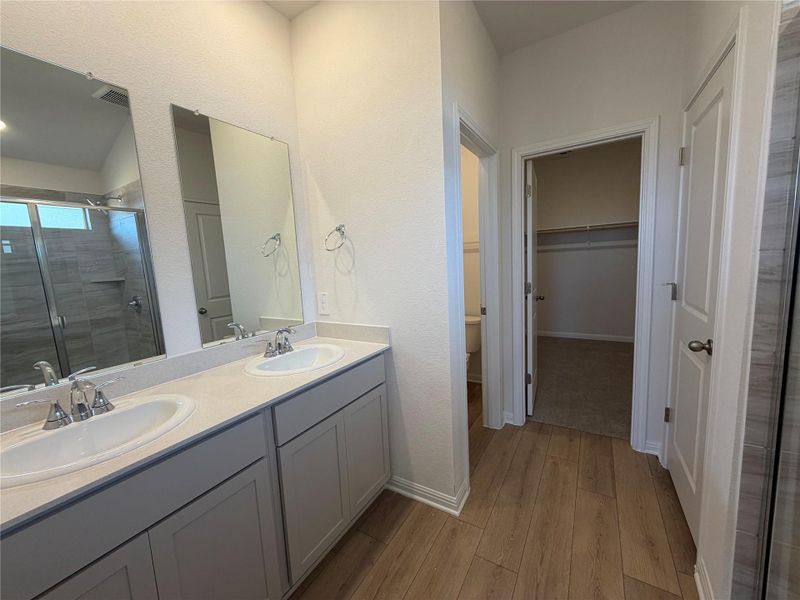Full bath featuring a stall shower, double vanity, a spacious closet, and light wood-style floors