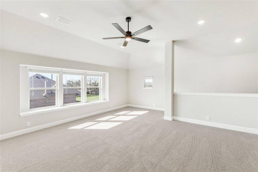 Empty room with carpet, ceiling fan, vaulted ceiling, and large windows letting in natural light Empty room with carpet, ceiling fan, vaulted ceiling, and large windows letting in natural light