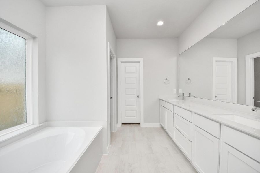 Escape to a spa-like oasis in this primary bathroom. Enjoy a walk-in shower with tile surround, a separate garden tub with custom detailing, and an elegant vanity featuring light countertops, modern hardware, and beautiful recessed lights. Experience luxury and relaxation in every detail.